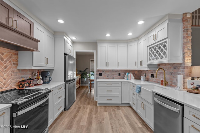 kitchen with stainless steel appliances, a sink, light countertops, light wood-style floors, and backsplash