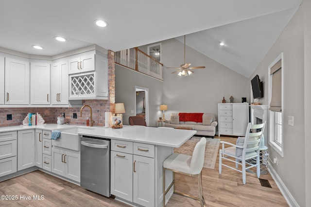 kitchen featuring stainless steel dishwasher, a sink, a peninsula, open floor plan, and tasteful backsplash