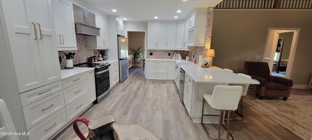 kitchen featuring electric range oven, a peninsula, a kitchen breakfast bar, light wood-style floors, and light countertops