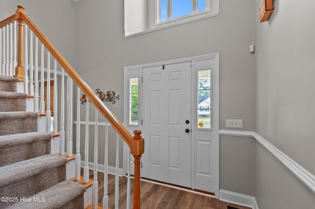 entryway featuring a towering ceiling, wood finished floors, stairway, and baseboards