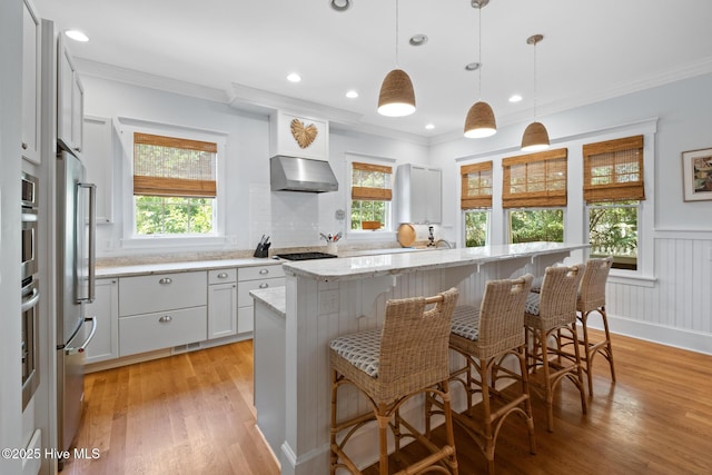 kitchen featuring under cabinet range hood, plenty of natural light, a breakfast bar, crown molding, and recessed lighting