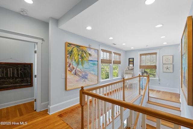 hall with an upstairs landing, baseboards, light wood-type flooring, and recessed lighting