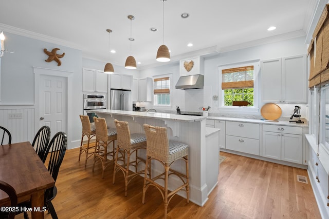 kitchen featuring crown molding, under cabinet range hood, high end fridge, a center island, and a kitchen bar