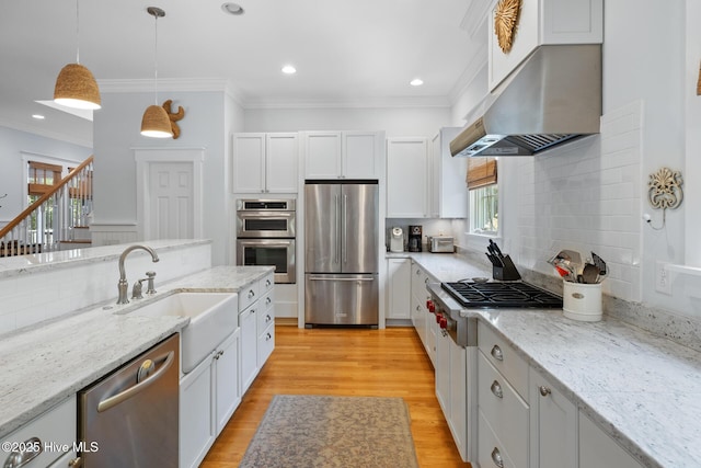 kitchen with appliances with stainless steel finishes, range hood, a sink, tasteful backsplash, and white cabinetry