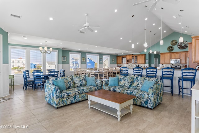 living room featuring a ceiling fan, wainscoting, a chandelier, light tile patterned floors, and high vaulted ceiling