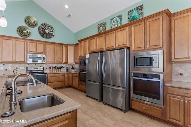 kitchen featuring appliances with stainless steel finishes, a sink, light stone countertops, tasteful backsplash, and brown cabinets