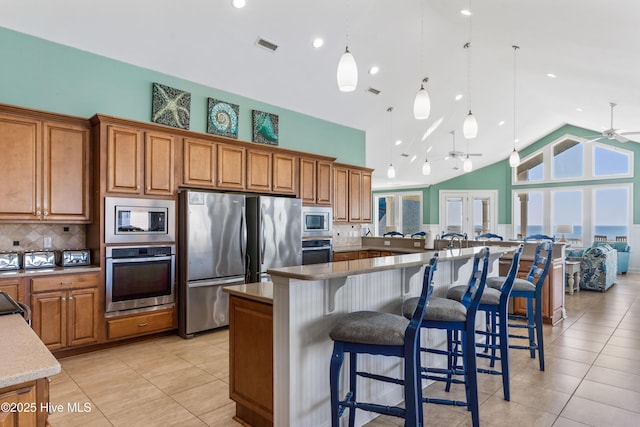 kitchen featuring appliances with stainless steel finishes, brown cabinetry, ceiling fan, and high vaulted ceiling