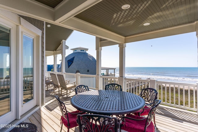 wooden deck with view of water and beach and outdoor dining space