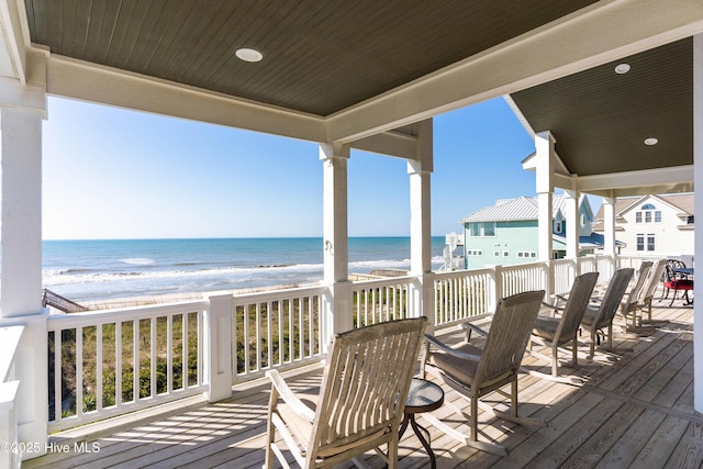 wooden deck with view of water and beach and outdoor dining area