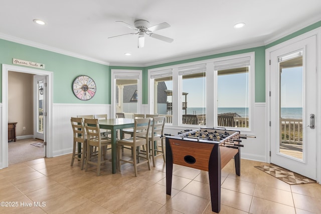 game room with healthy amount of natural light, ceiling fan, a water view, a wainscoted wall, and light tile patterned flooring