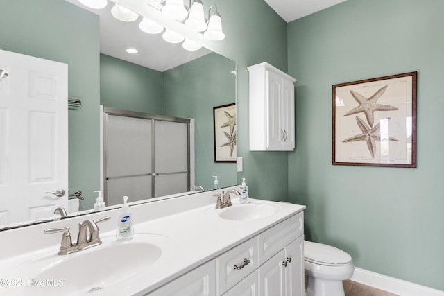 full bathroom with toilet, double vanity, a shower with shower door, and baseboards