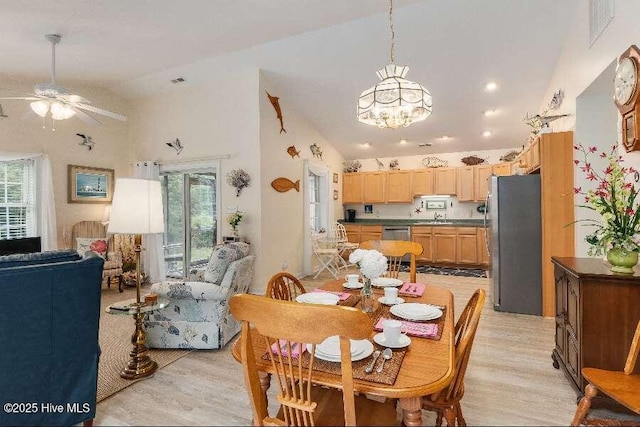 dining room featuring healthy amount of natural light, a ceiling fan, a chandelier, light wood-style flooring, and high vaulted ceiling