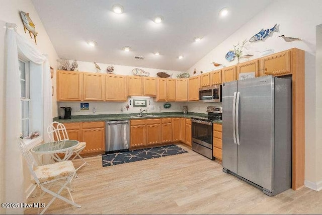 kitchen featuring appliances with stainless steel finishes, lofted ceiling, light wood finished floors, dark countertops, and a sink