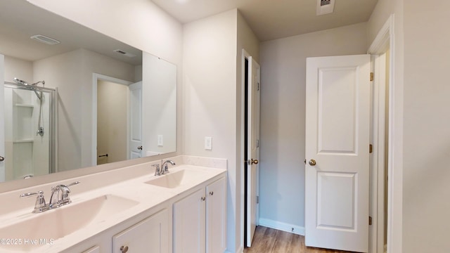 full bathroom with a shower with door, double vanity, wood finished floors, and baseboards