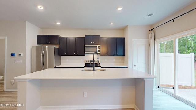 kitchen featuring stainless steel appliances, light wood-type flooring, light countertops, baseboards, and an island with sink