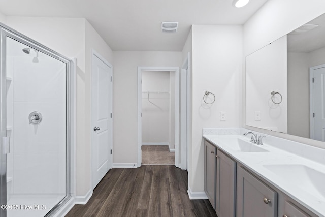 full bathroom with a stall shower, wood finished floors, double vanity, baseboards, and a spacious closet