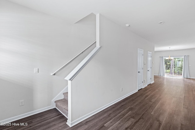 unfurnished living room with a chandelier, dark wood-style flooring, stairway, and baseboards