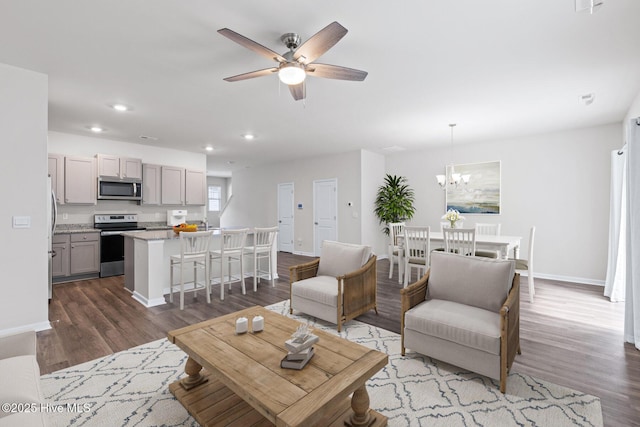 living area with dark wood-type flooring, recessed lighting, baseboards, ceiling fan, and a chandelier