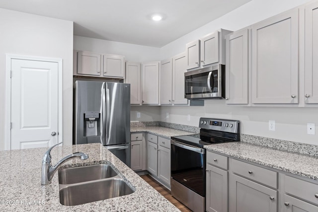 kitchen with stainless steel appliances, a sink, gray cabinets, light stone countertops, and recessed lighting