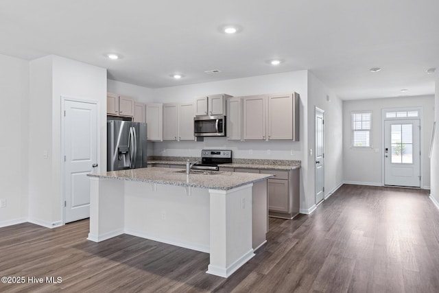 kitchen with stainless steel appliances, a sink, dark wood-style flooring, gray cabinets, and an island with sink