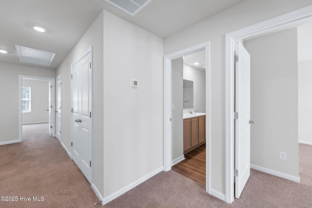 hall featuring carpet, attic access, baseboards, a sink, and recessed lighting