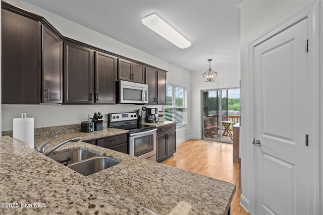 kitchen with appliances with stainless steel finishes, a sink, light wood-style floors, dark brown cabinets, and light stone counters