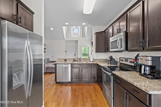 kitchen with appliances with stainless steel finishes, dark brown cabinetry, light wood-style floors, a peninsula, and a sink