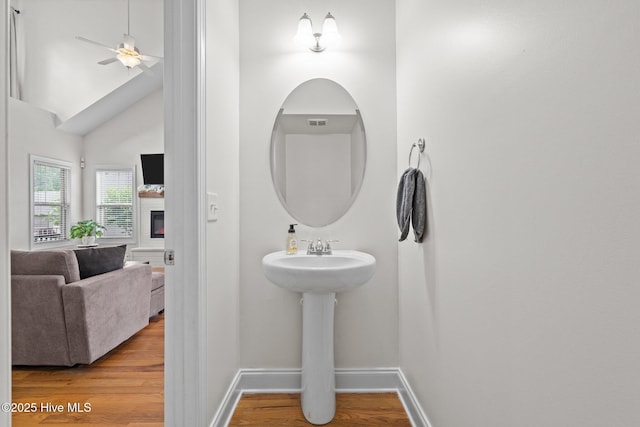 bathroom with wood finished floors, a ceiling fan, baseboards, a glass covered fireplace, and vaulted ceiling
