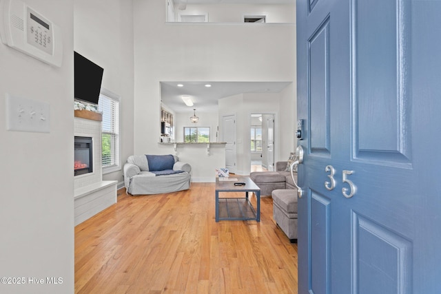 entrance foyer with light wood-style floors, a glass covered fireplace, a high ceiling, and baseboards