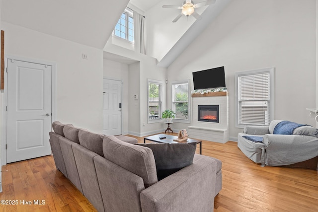 living area featuring a towering ceiling, plenty of natural light, ceiling fan, and light wood-style floors