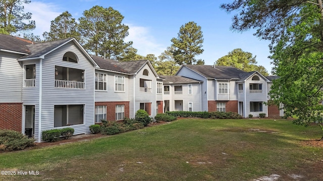 view of front of house with a front lawn, brick siding, and roof with shingles