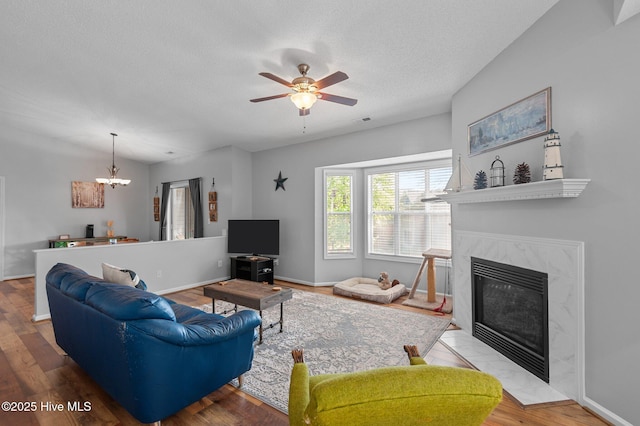 living area featuring a high end fireplace, a chandelier, ceiling fan, wood finished floors, and a textured ceiling