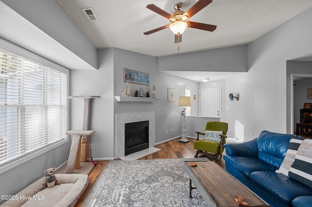 living area featuring wood finished floors, ceiling fan, a textured ceiling, a high end fireplace, and baseboards