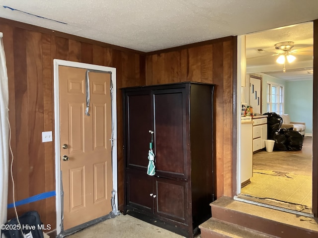 entrance foyer with ceiling fan, wood walls, and a textured ceiling