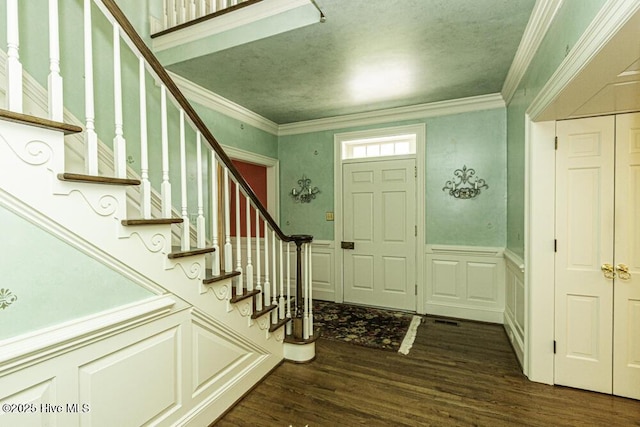 entryway with dark wood finished floors, a decorative wall, stairs, ornamental molding, and wainscoting