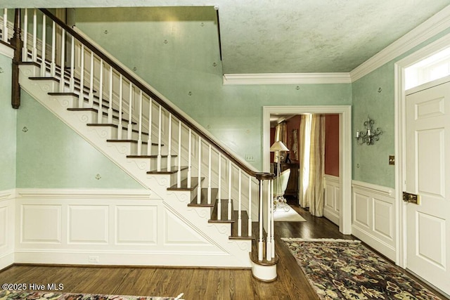 entrance foyer with stairs, a wainscoted wall, wood finished floors, crown molding, and a decorative wall