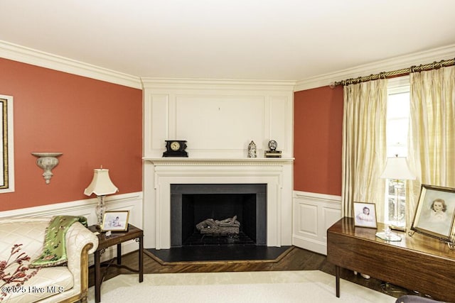 living area with wood finished floors, a fireplace, ornamental molding, and a wainscoted wall
