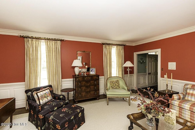 living area featuring crown molding, a wainscoted wall, carpet flooring, and a decorative wall