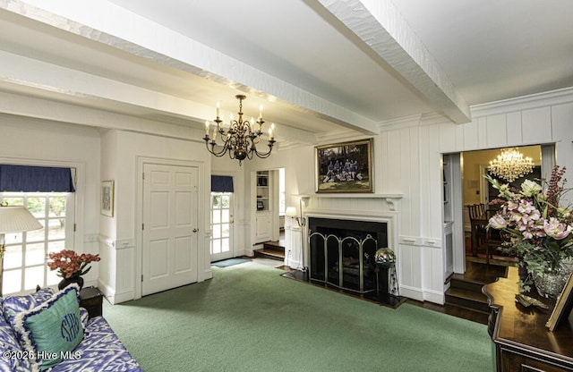 living room featuring a chandelier, beamed ceiling, a decorative wall, and a fireplace with raised hearth