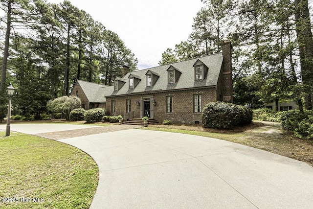 cape cod house with a chimney, brick siding, a front yard, driveway, and roof with shingles