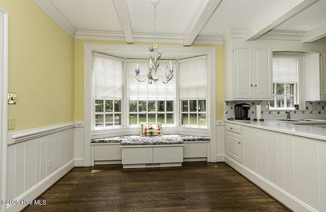unfurnished dining area with beamed ceiling, a chandelier, a sink, dark wood finished floors, and wainscoting