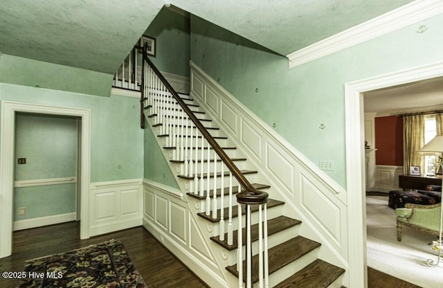 stairway with wood finished floors, a wainscoted wall, crown molding, and a decorative wall