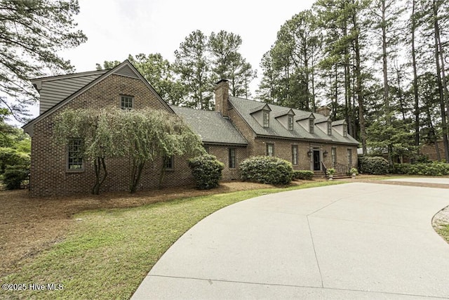 new england style home featuring a chimney, brick siding, a front lawn, and driveway