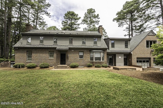 view of front of house with a chimney, an attached garage, brick siding, a front lawn, and roof with shingles