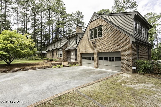 view of side of property with an attached garage, driveway, brick siding, and a chimney