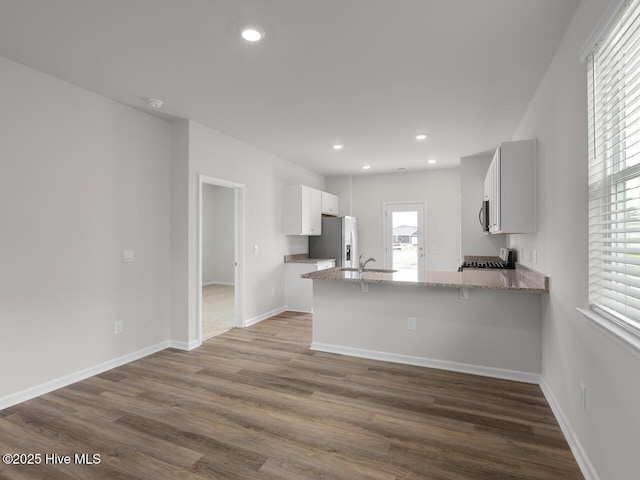 kitchen featuring a peninsula, stainless steel refrigerator with ice dispenser, light stone countertops, a sink, and dark wood-style flooring