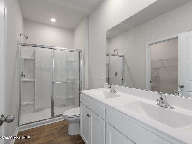 bathroom with a shower stall, wood finished floors, toilet, double vanity, and recessed lighting