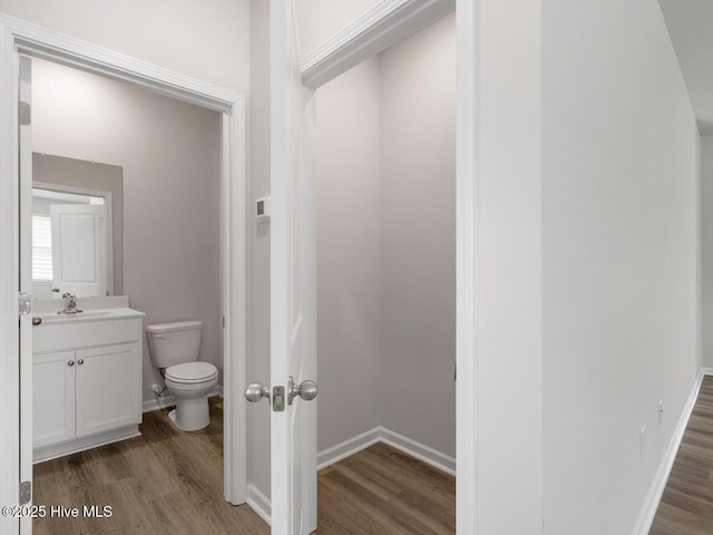 half bath featuring wood finished floors, toilet, vanity, and baseboards