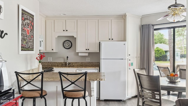 227 Foxkroft Dr Unit 9, Foxfire Village, NC 27281 - kitchen with white appliances, light wood-style floors, a textured ceiling, a breakfast bar area, and white cabinetry