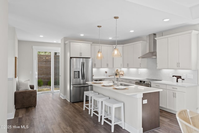 kitchen with stainless steel appliances, wall chimney exhaust hood, a sink, decorative backsplash, and white cabinetry